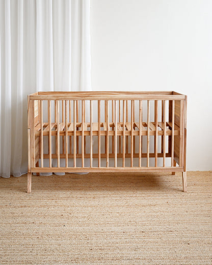 Wooden crib in a room with white curtains and a beige carpet.