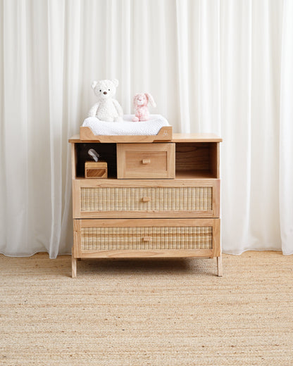 Wooden changing table with toys on top against a white curtain background