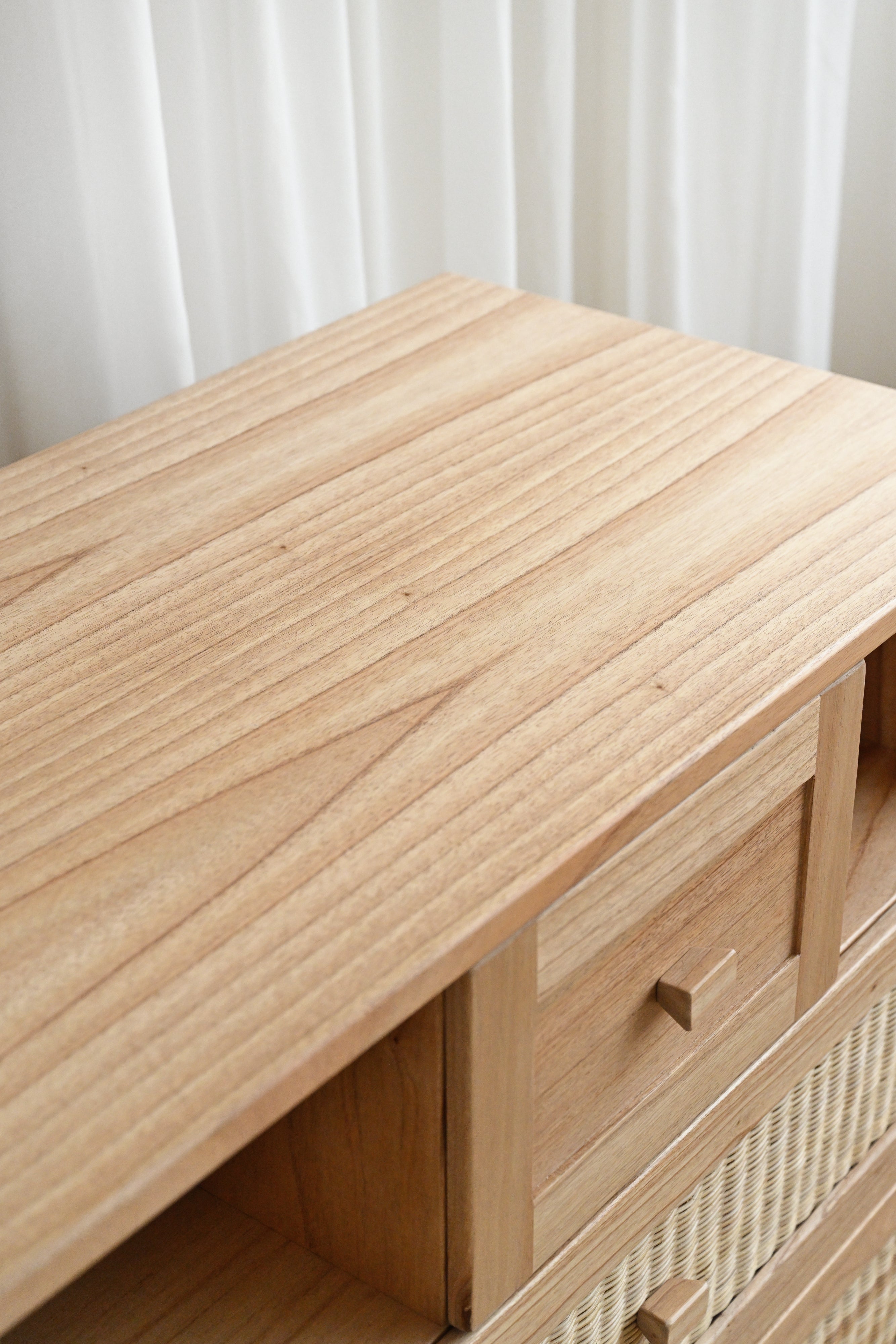 Wooden drawer unit with a textured surface against a white curtain background