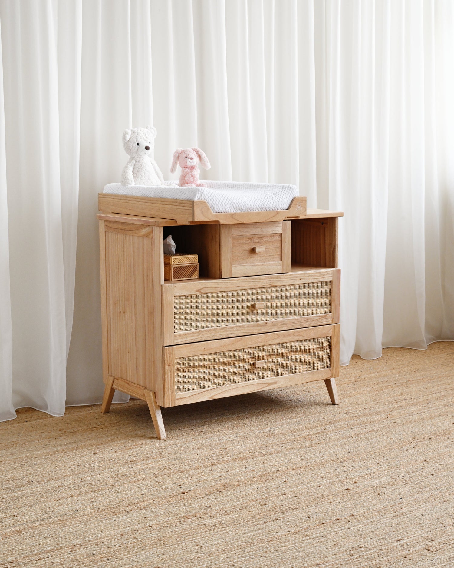 Wooden dresser with wicker drawers against a white curtain background