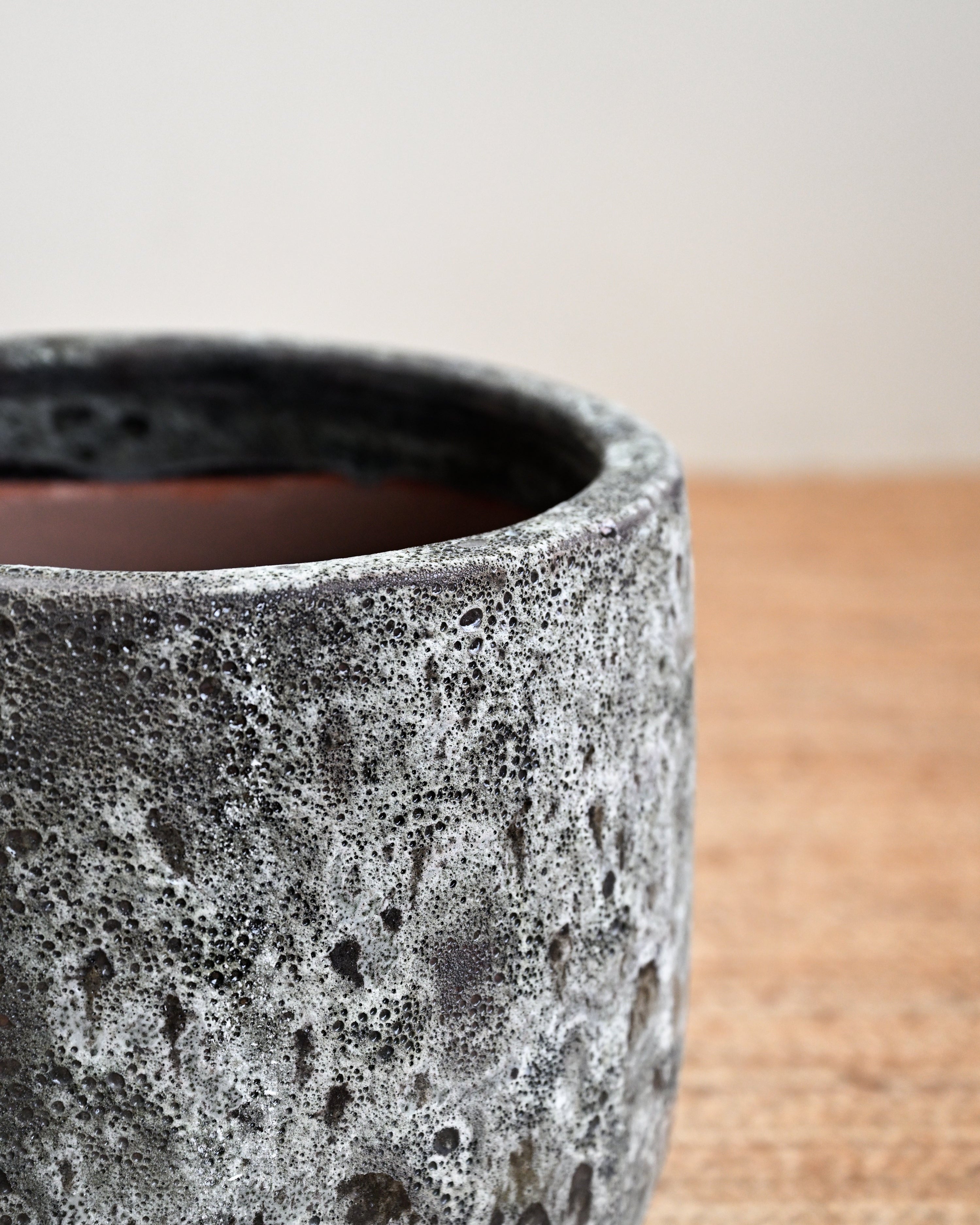 Textured ceramic pot on a wooden surface with a neutral background