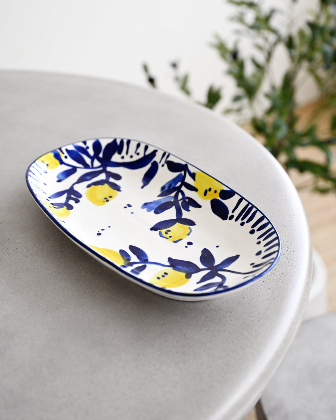 An oval ceramic plate with a blue and yellow lemon pattern, resting on a light gray table with a blurred background.