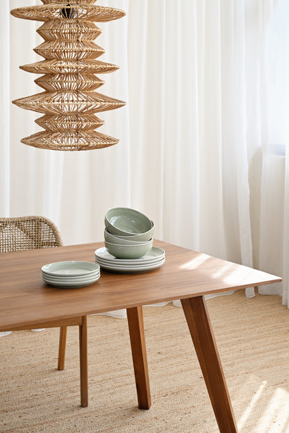 Wooden table with green ceramic bowls and a hanging woven lamp in a bright room.