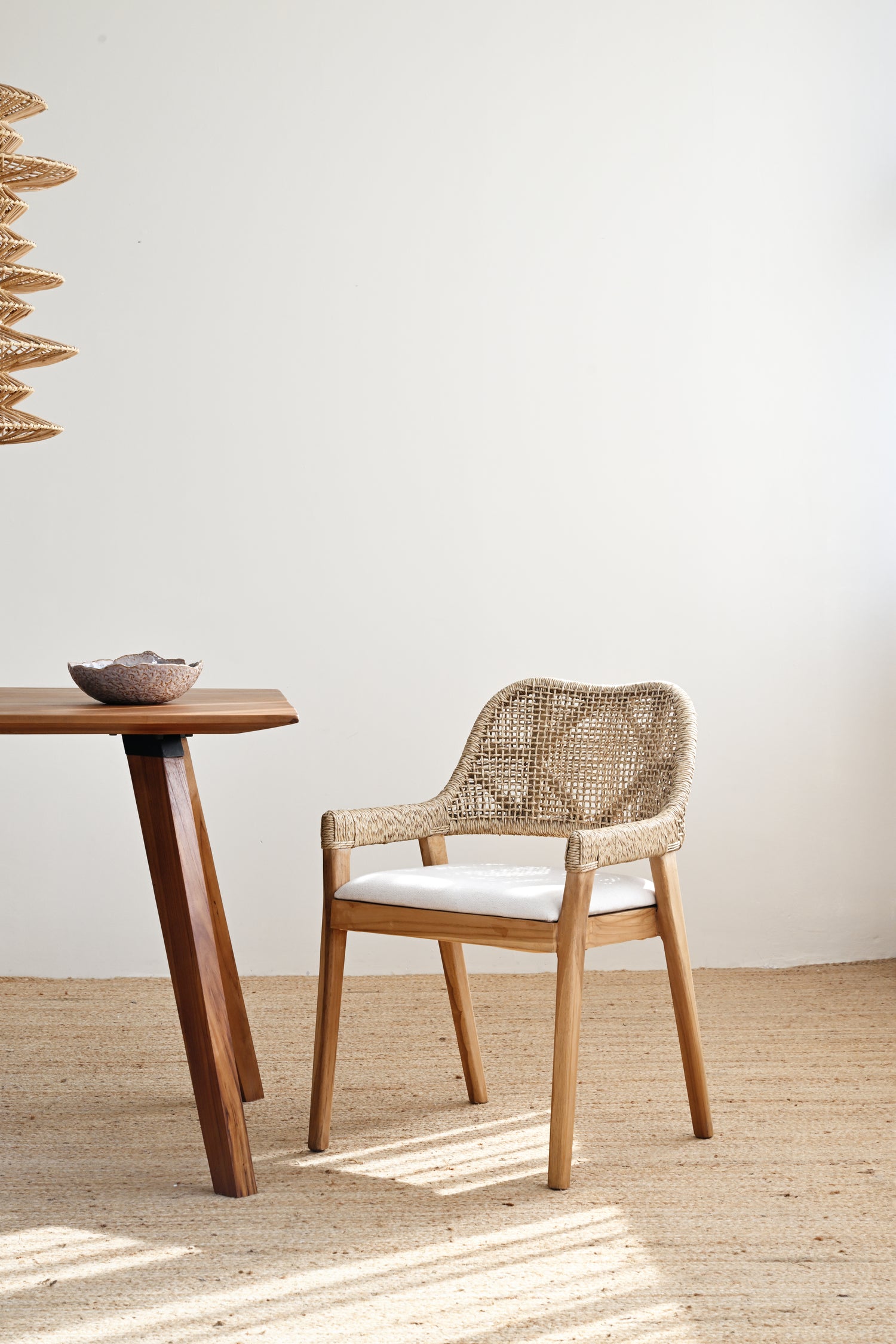 Woven chair and wooden table in a minimalistic room with a white wall and wooden floor.