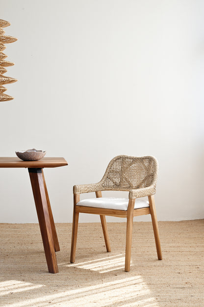 Woven chair and wooden table in a minimalistic room with a white wall and wooden floor.