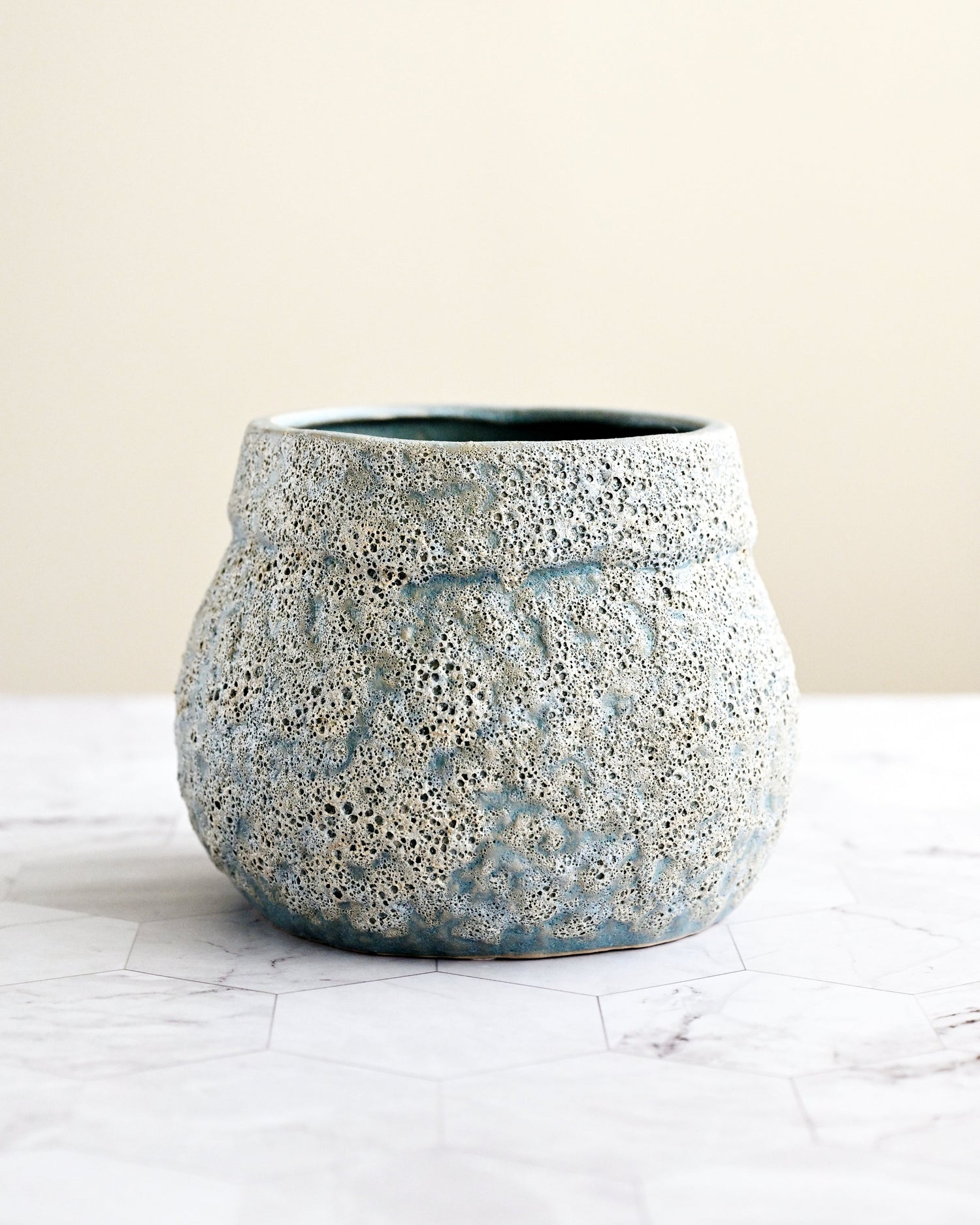 Speckled blue and gray ceramic pot on a white surface with a beige background