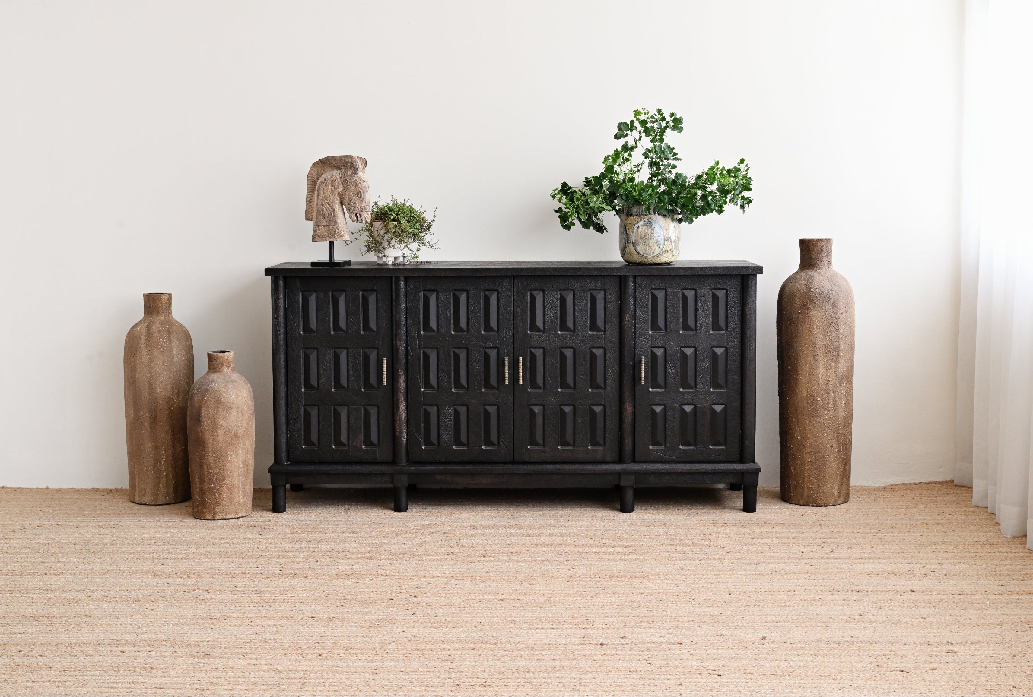 Black wooden sideboard with decorative vases and plants in a minimalistic room.