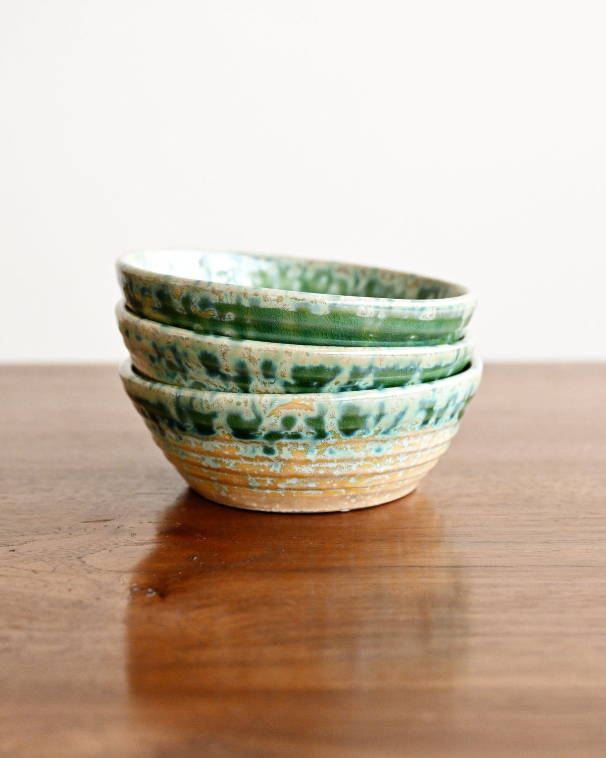 Three stacked ceramic bowls with a green and white marbled pattern and a natural beige rim, displayed on a wooden table against a white background.