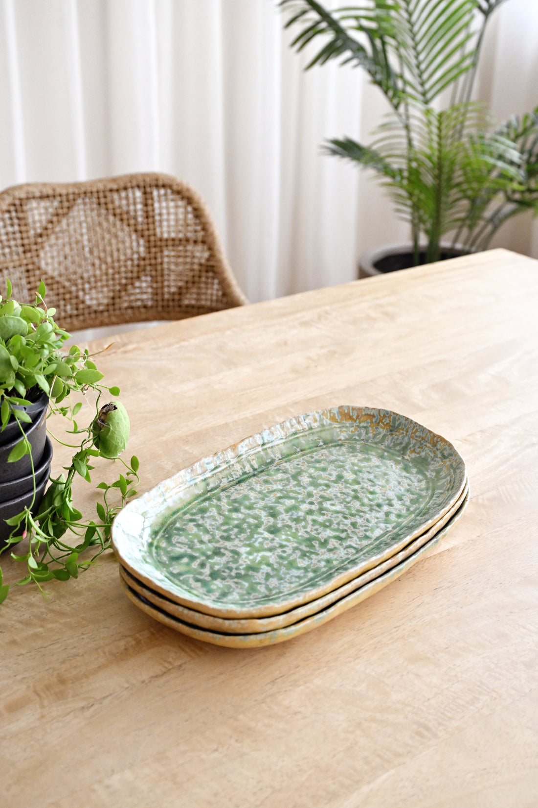Stack of ceramic trays with green speckled pattern on a wooden table.