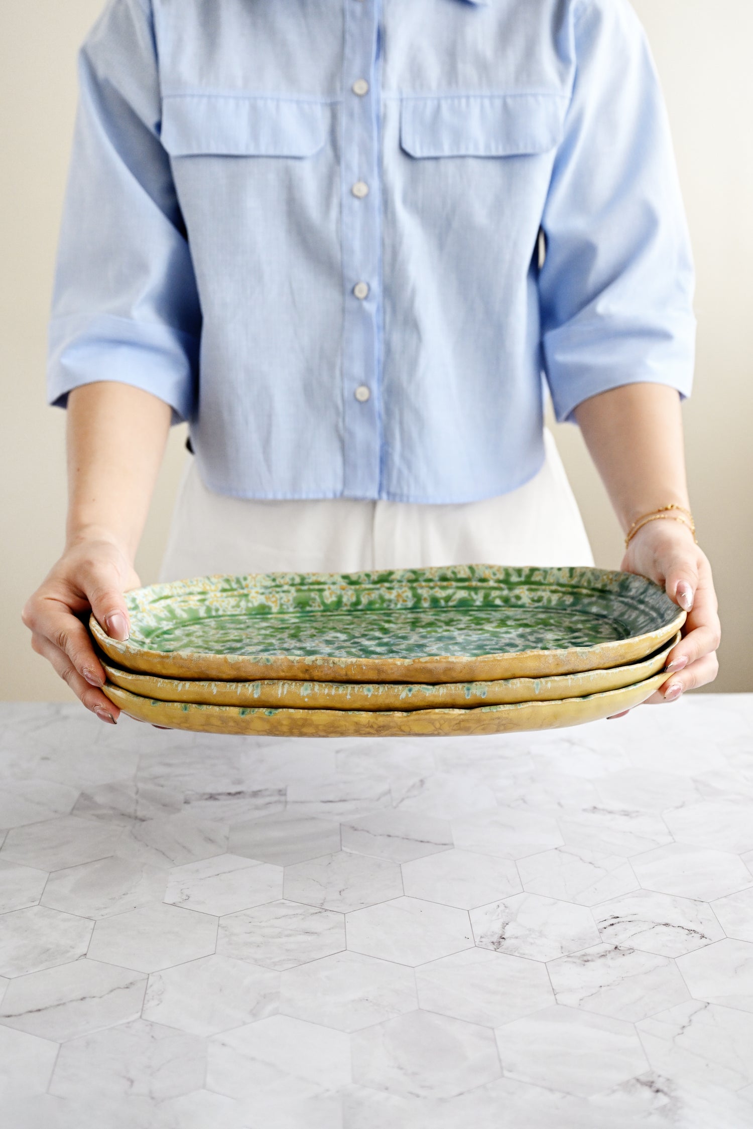 Person holding three ceramic plates on a marble surface