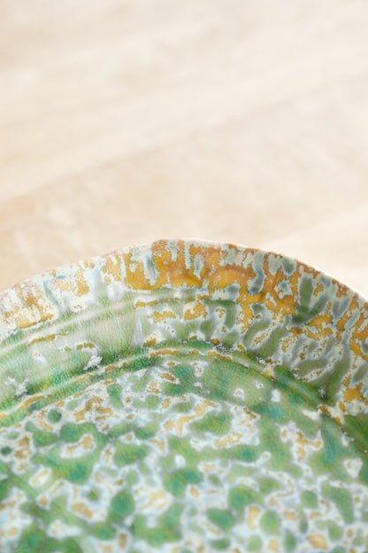 Close-up of a ceramic plate with green and yellow glaze on a beige background
