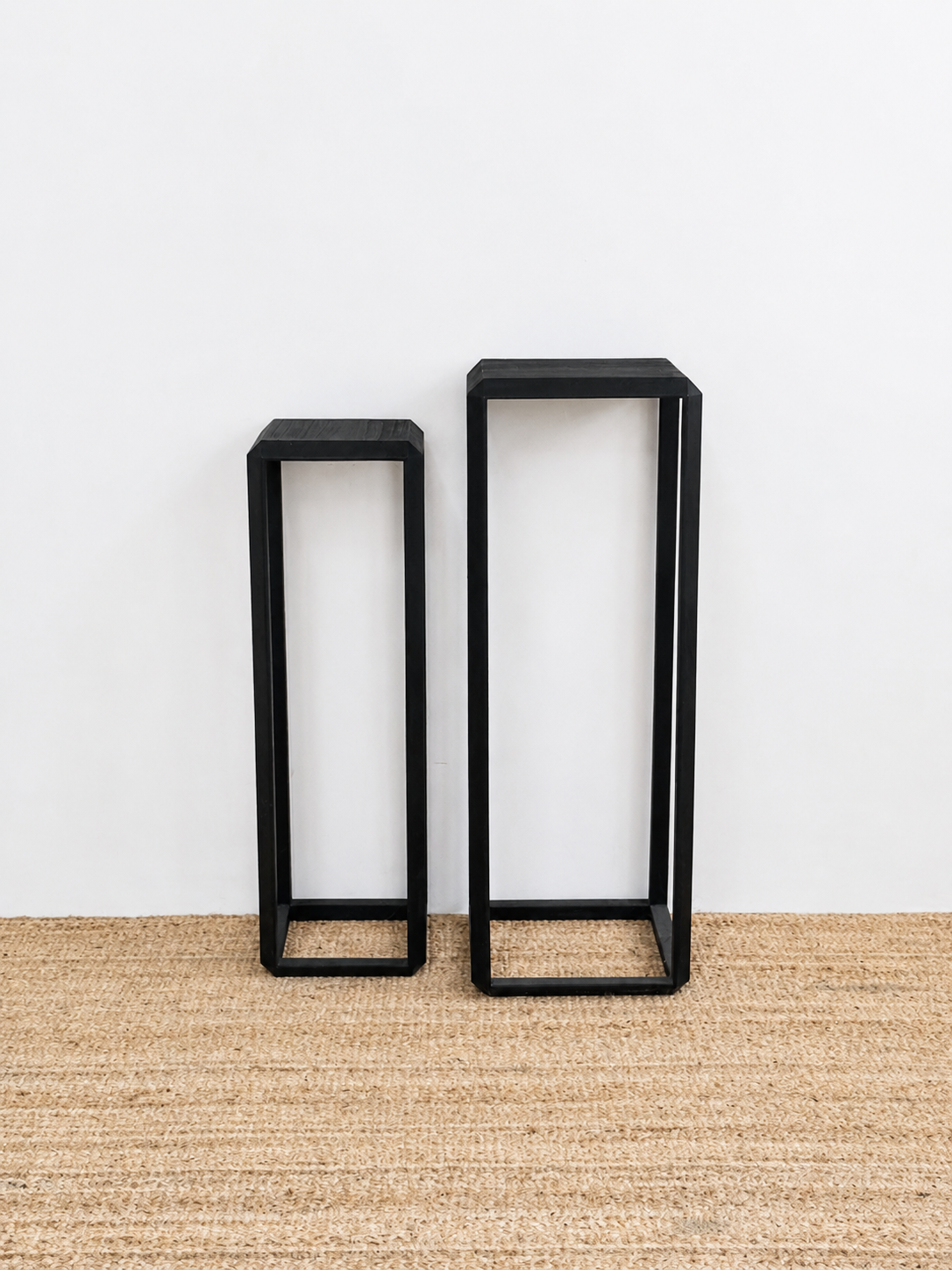 Two black rectangular shelves on a beige carpet with a white wall background