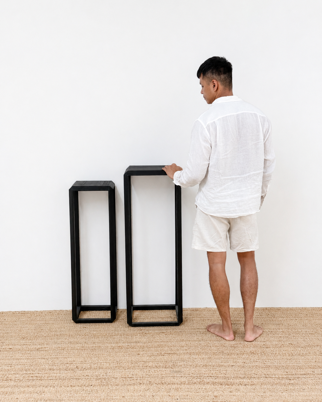 Man standing next to two black side tables on a beige carpet with a white wall background