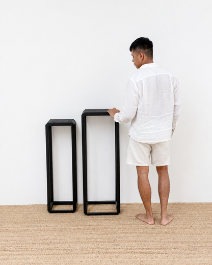 Man standing next to two black side tables on a beige carpet with a white wall background
