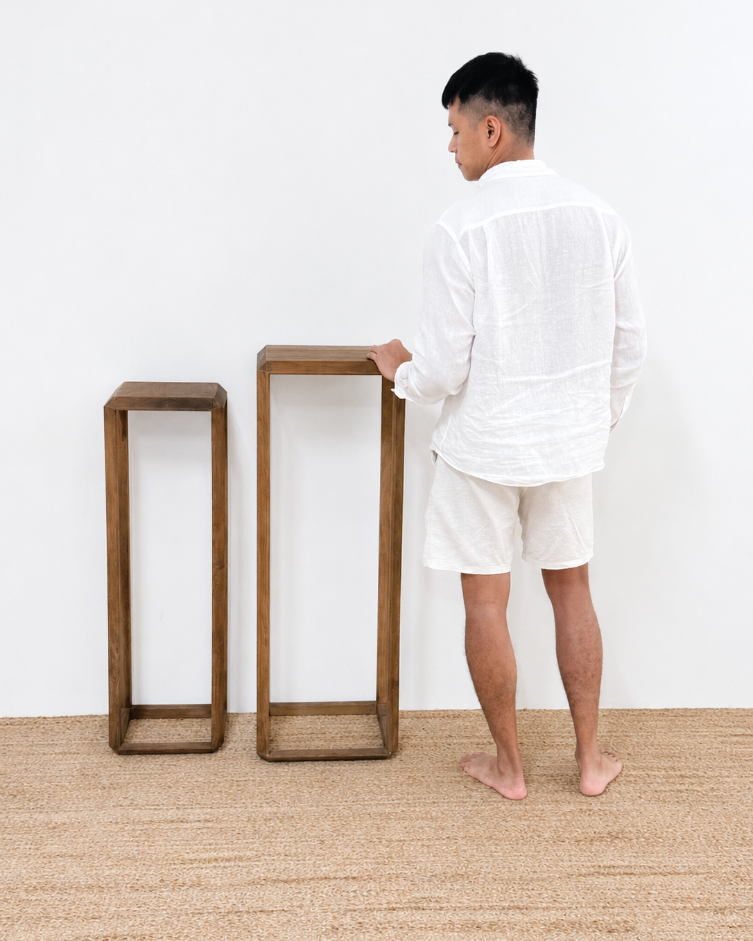Man in a white robe standing next to two wooden stools on a beige carpet.