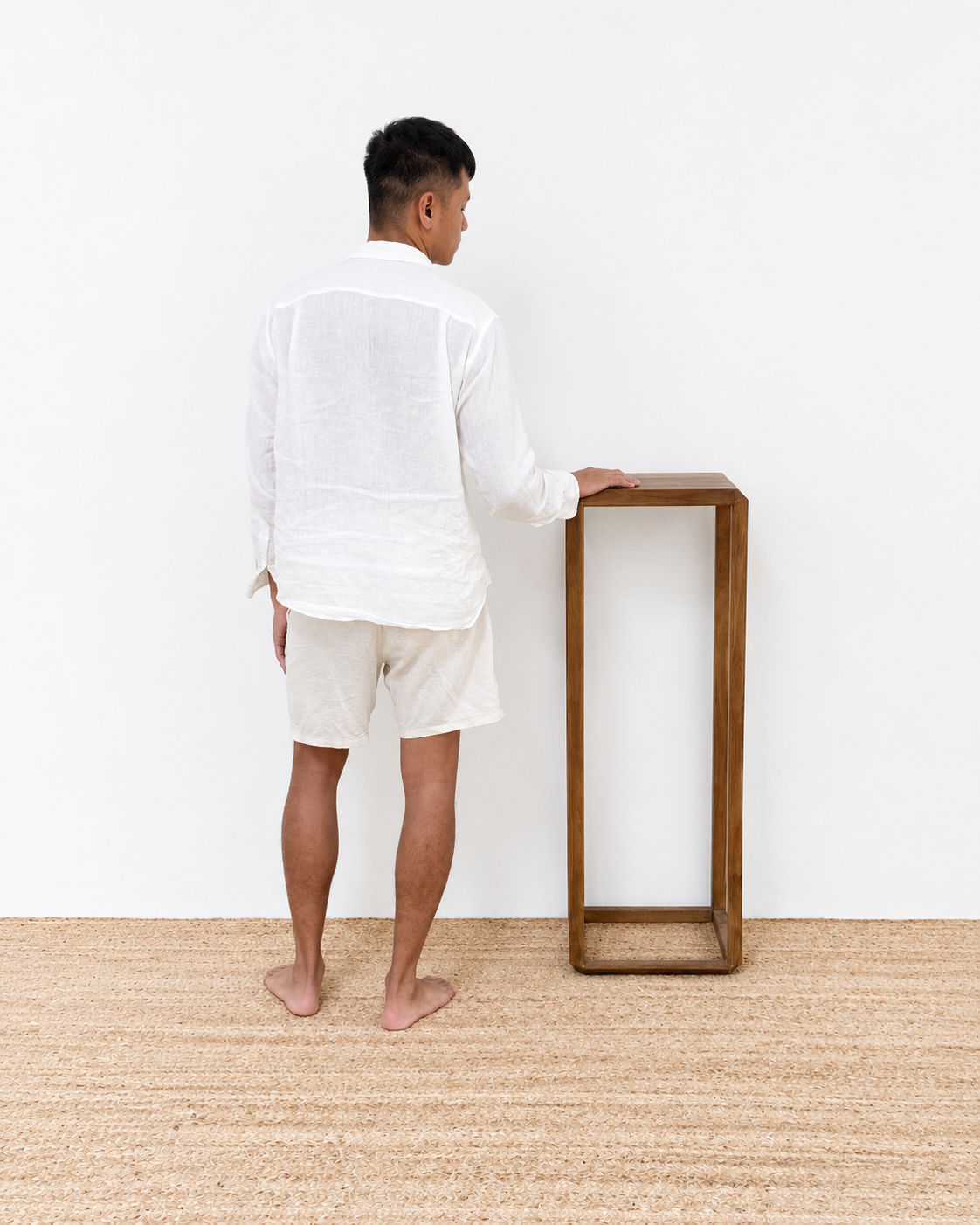 Person standing next to a wooden side table in a minimalistic room.