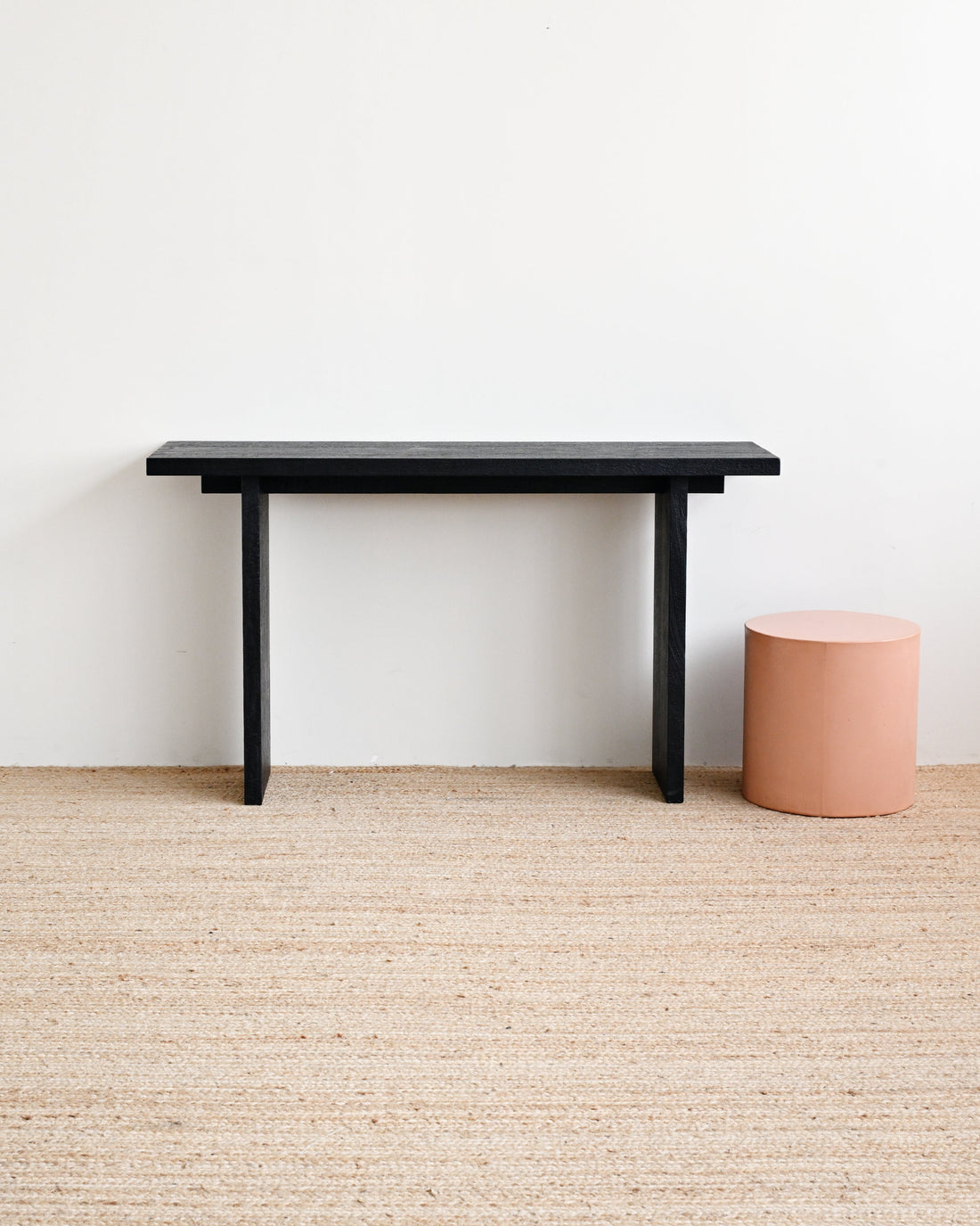 Black table and pink cylindrical object on a beige carpet with a white wall background