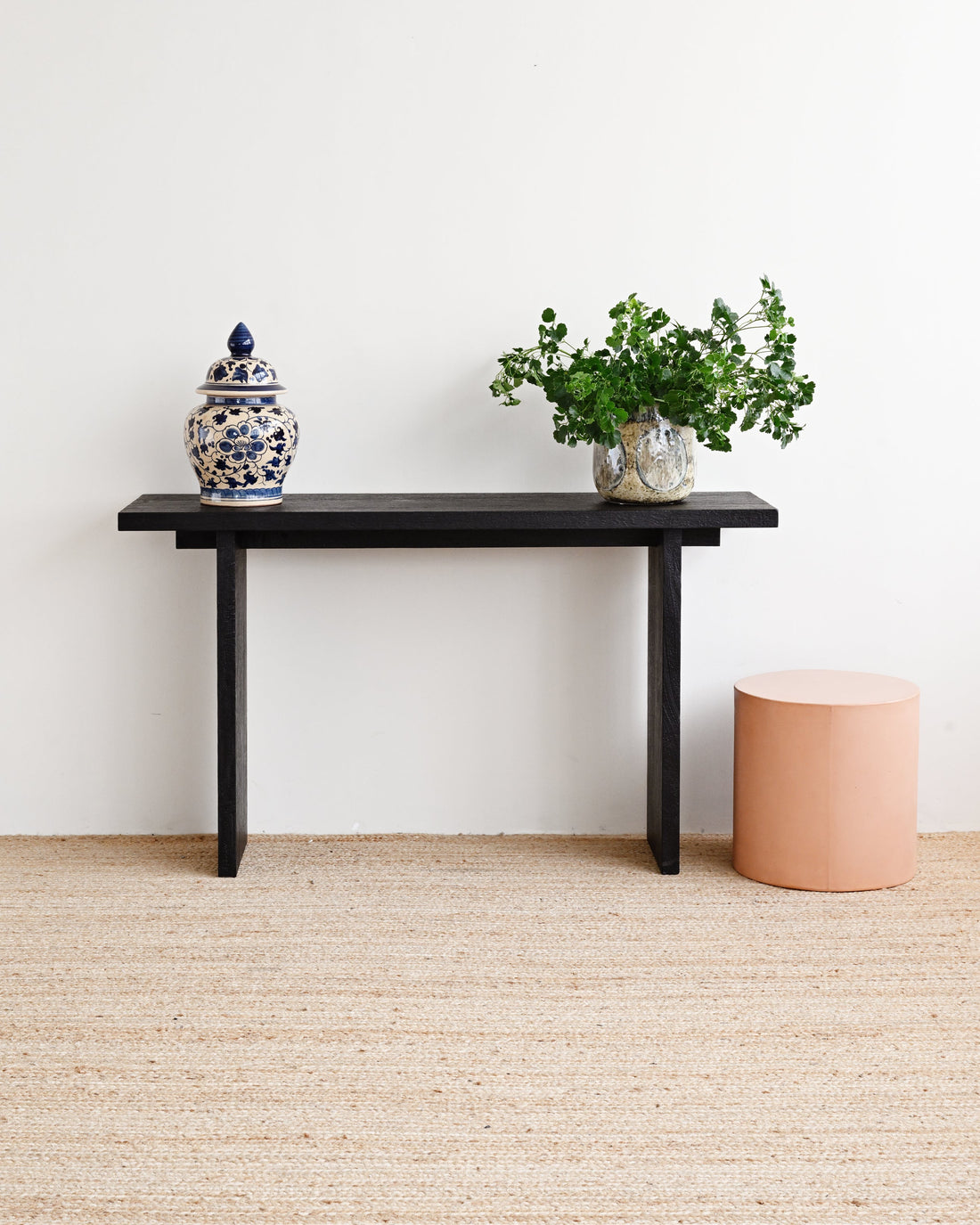 Minimalist room with a black console table, decorative jar, and plant against a white wall.