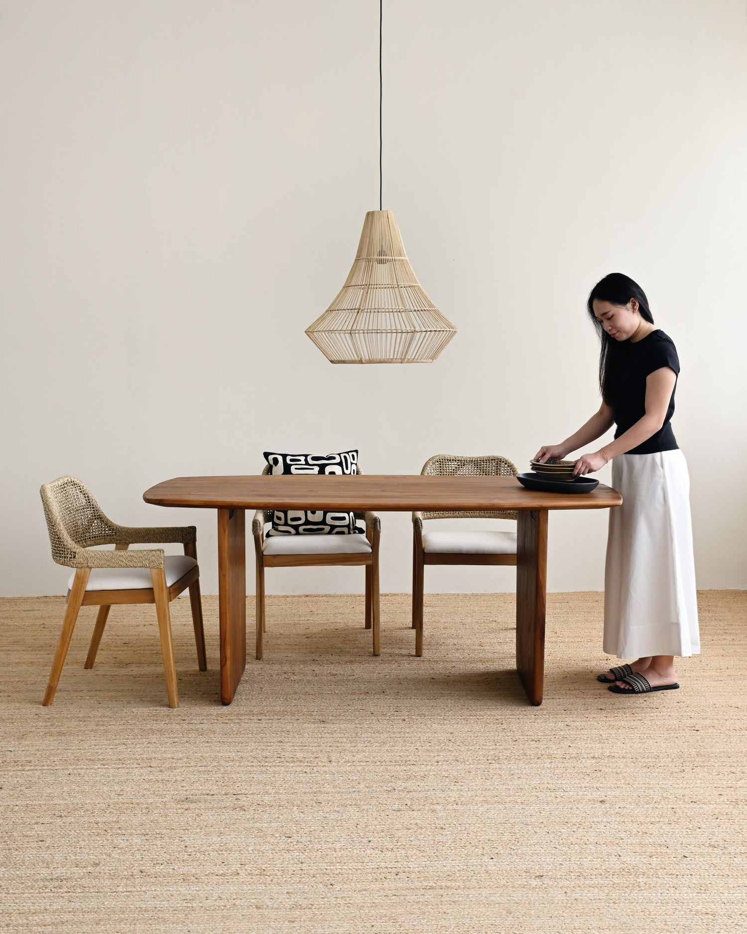 Woman setting a table in a minimalistic room with wooden furniture and a pendant light.