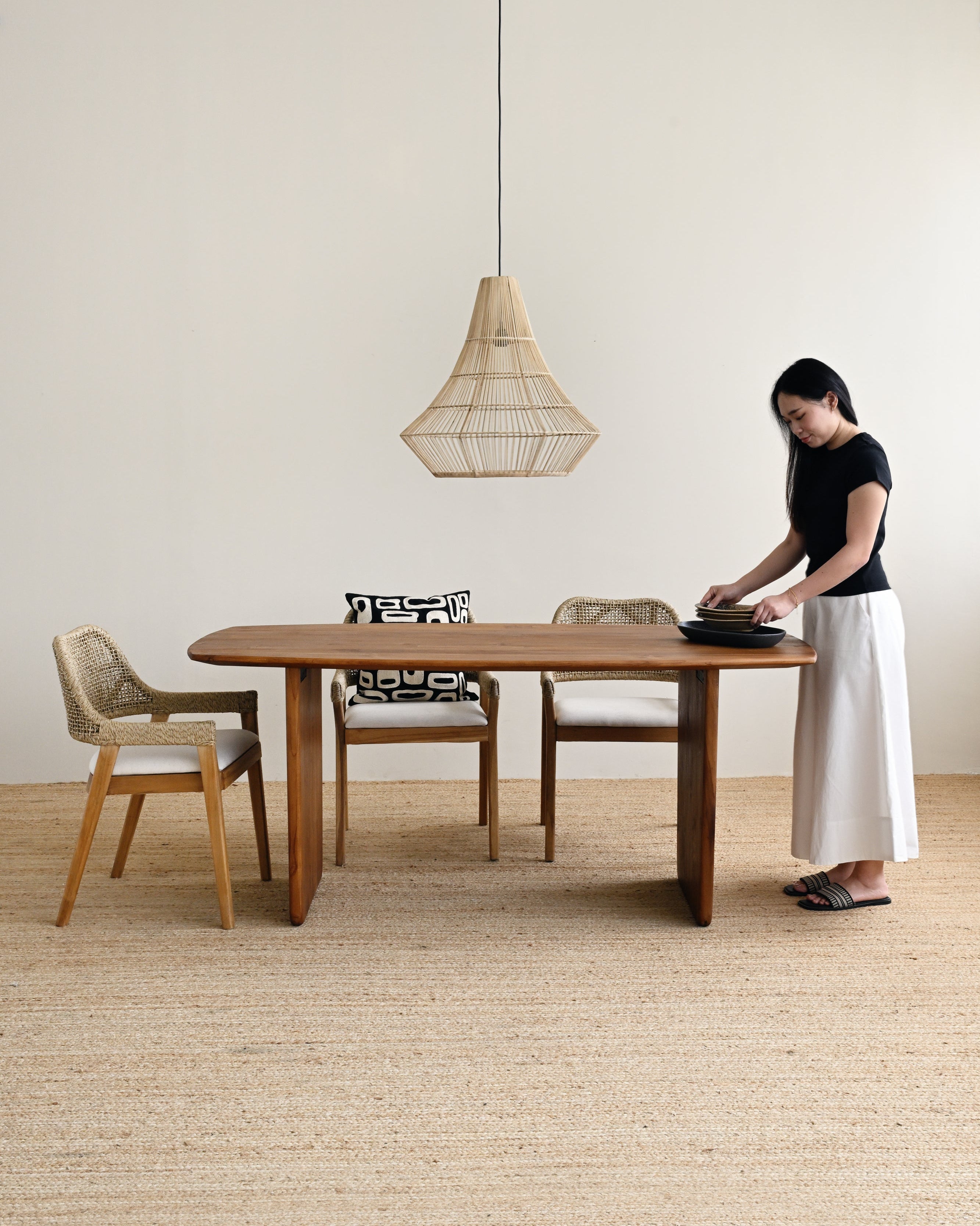 Woman setting a table in a minimalistic room with wooden furniture and a pendant light.