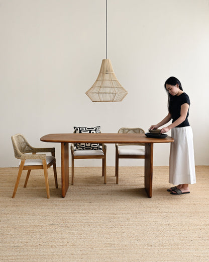 Woman setting a table in a minimalistic room with wooden furniture and a pendant light.