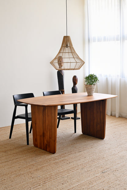 Modern wooden dining table with black chairs and a hanging lamp in a bright room.