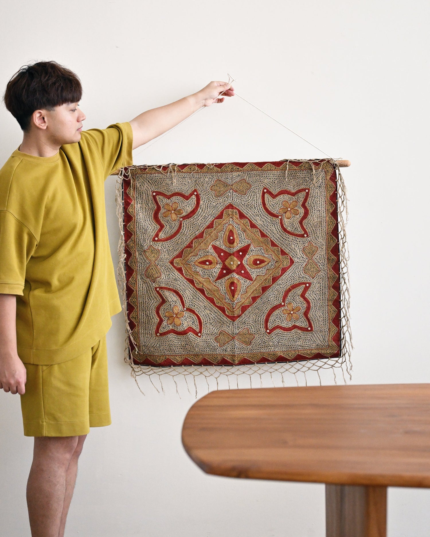Person holding a decorative rug with intricate patterns in a room with a wooden table.