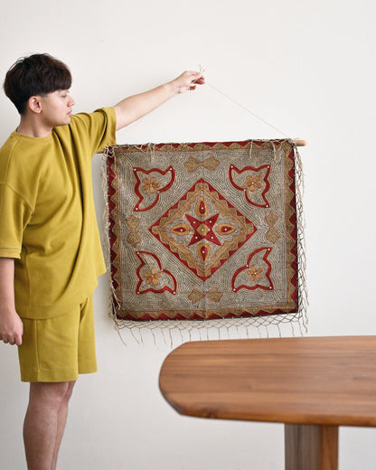 Person holding a decorative rug with intricate patterns in a room with a wooden table.