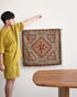 Person holding a decorative rug with intricate patterns in a room with a wooden table.