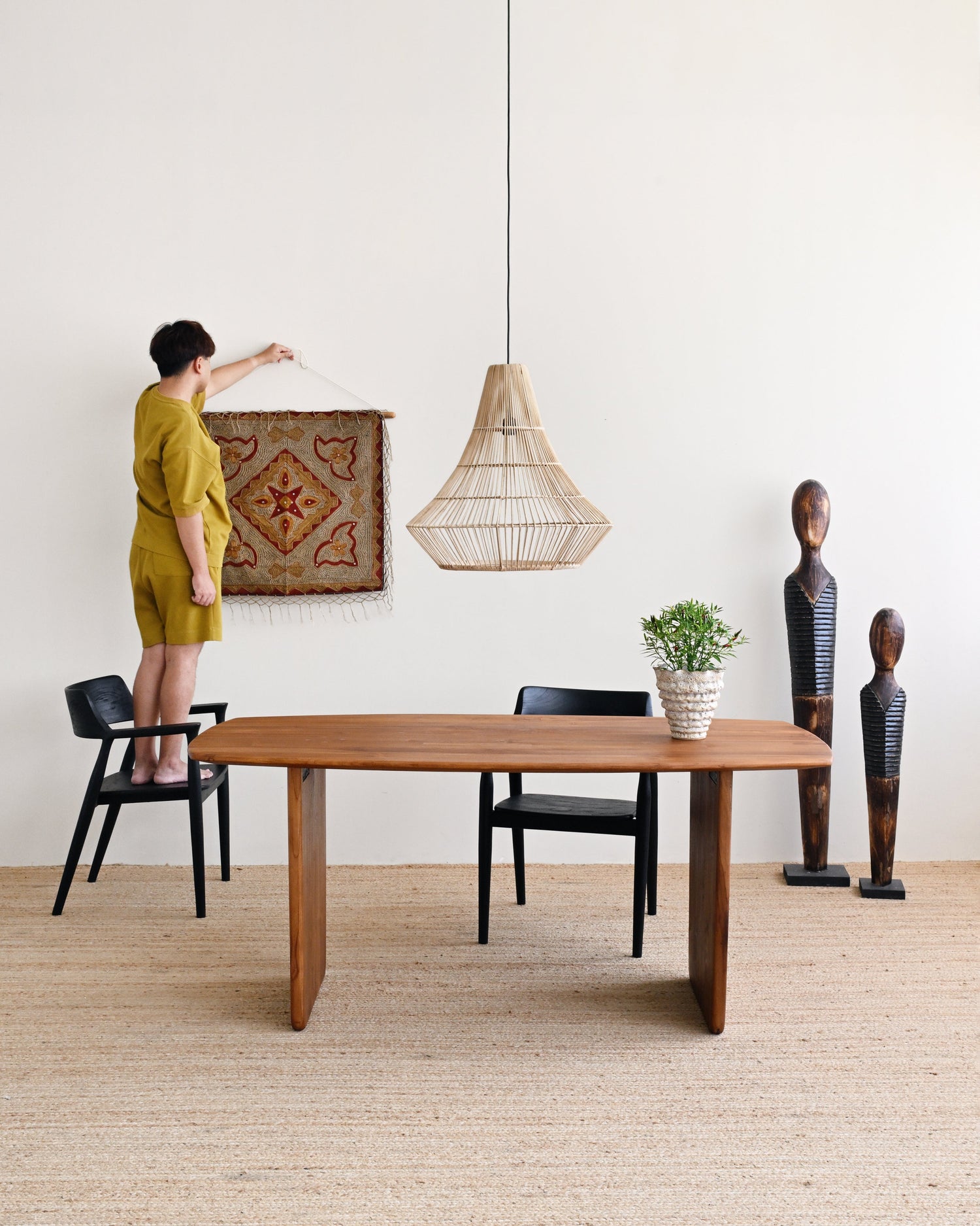 Person hanging a decorative rug above a wooden dining table in a modern room.