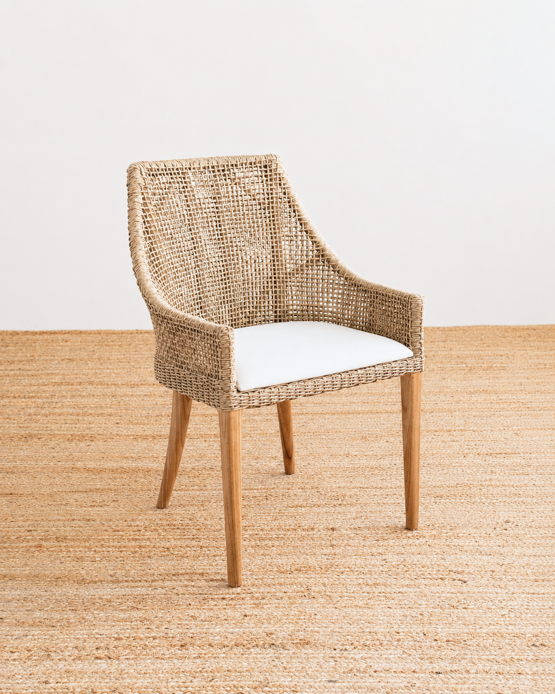 Wicker chair with a white cushion on a textured beige floor.