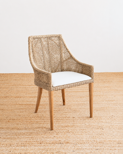 Wicker chair with a white cushion on a textured beige floor.