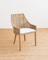 Wicker chair with a white cushion on a textured beige floor.