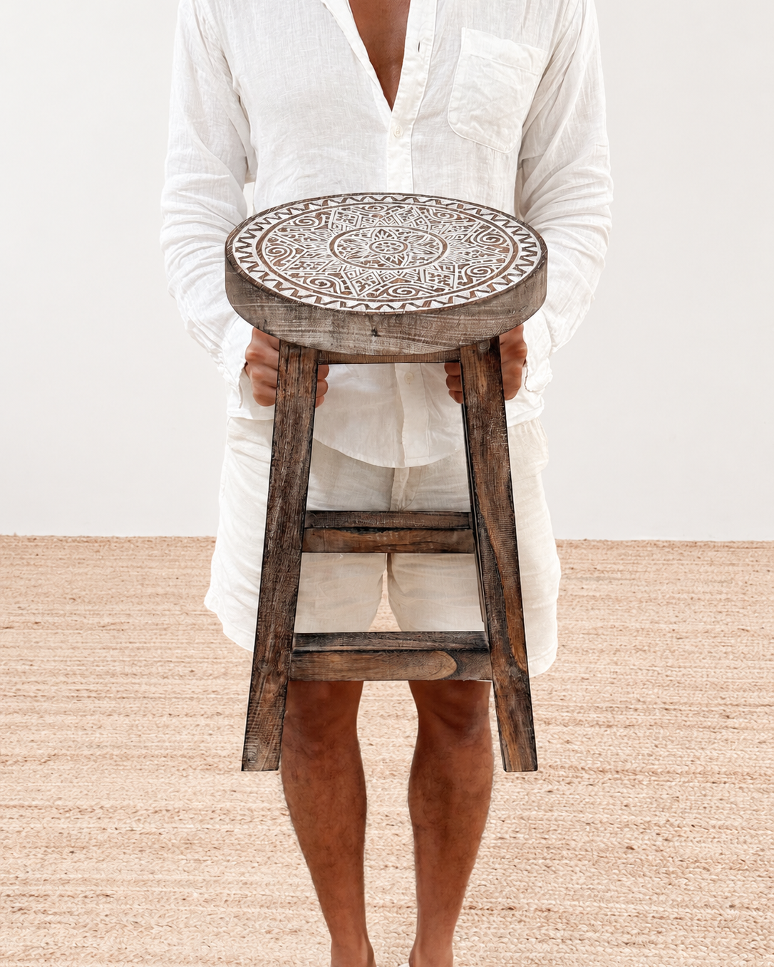 Person holding a wooden stool with intricate designs on a plain background