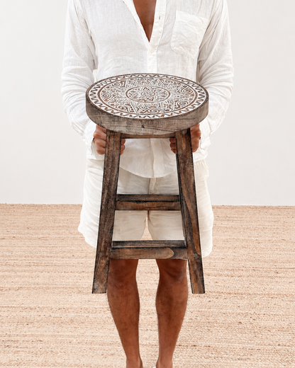 Person holding a wooden stool with intricate designs on a plain background