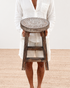 Person holding a wooden stool with intricate designs on a plain background