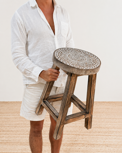 Person holding a wooden stool with intricate design on a light background