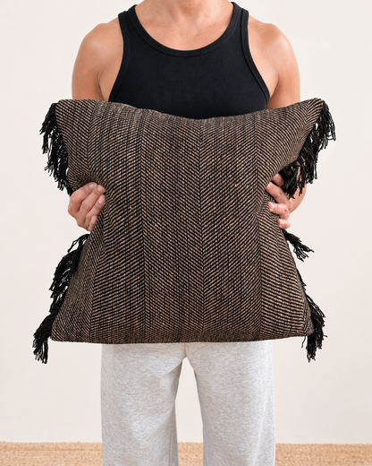 Person holding a brown woven bag with black fringes on a plain background