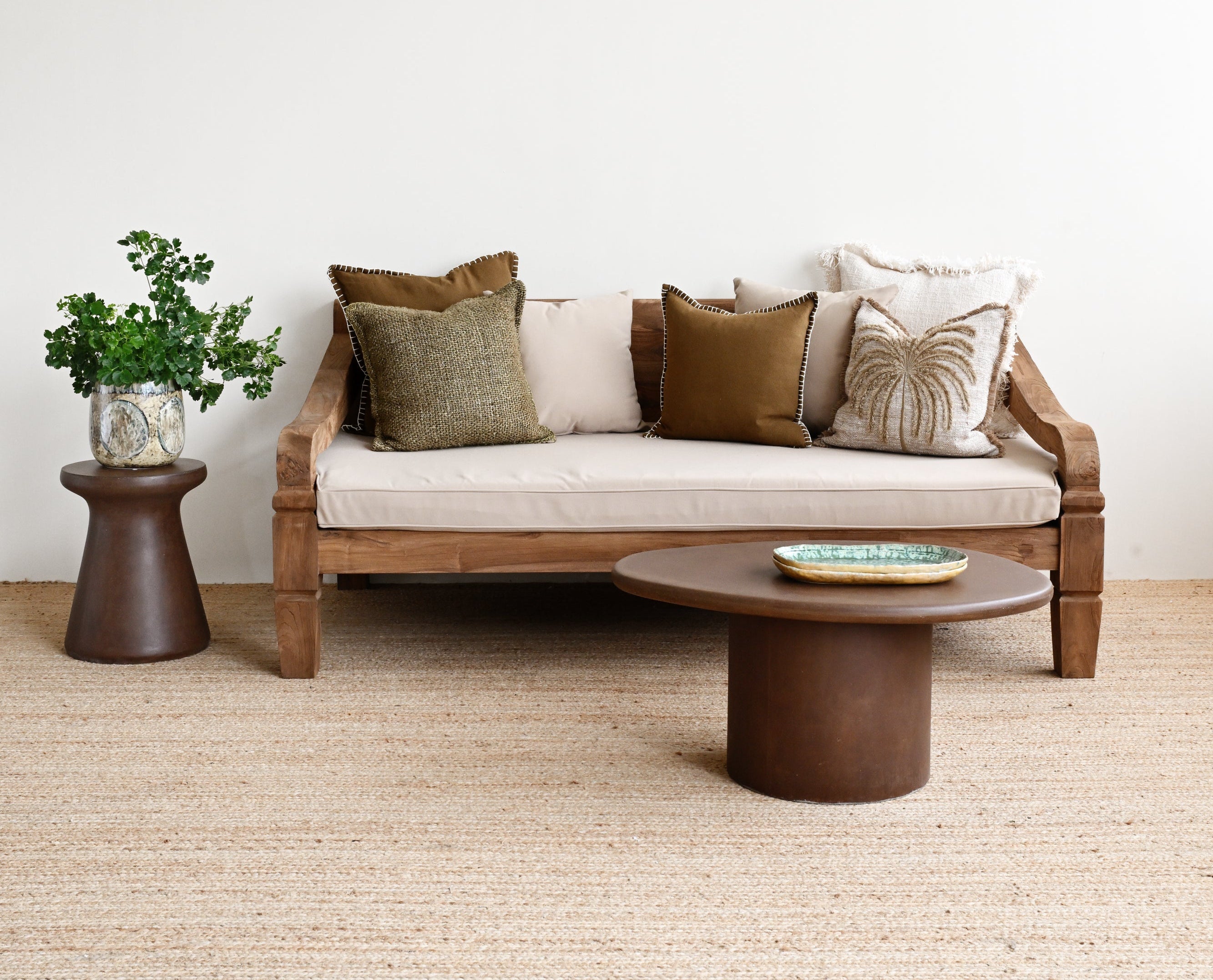 Modern living room with a wooden sofa, round coffee table, and decorative pillows on a light-colored carpet.