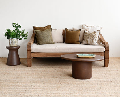 Modern living room with a wooden sofa, round coffee table, and decorative pillows on a light-colored carpet.