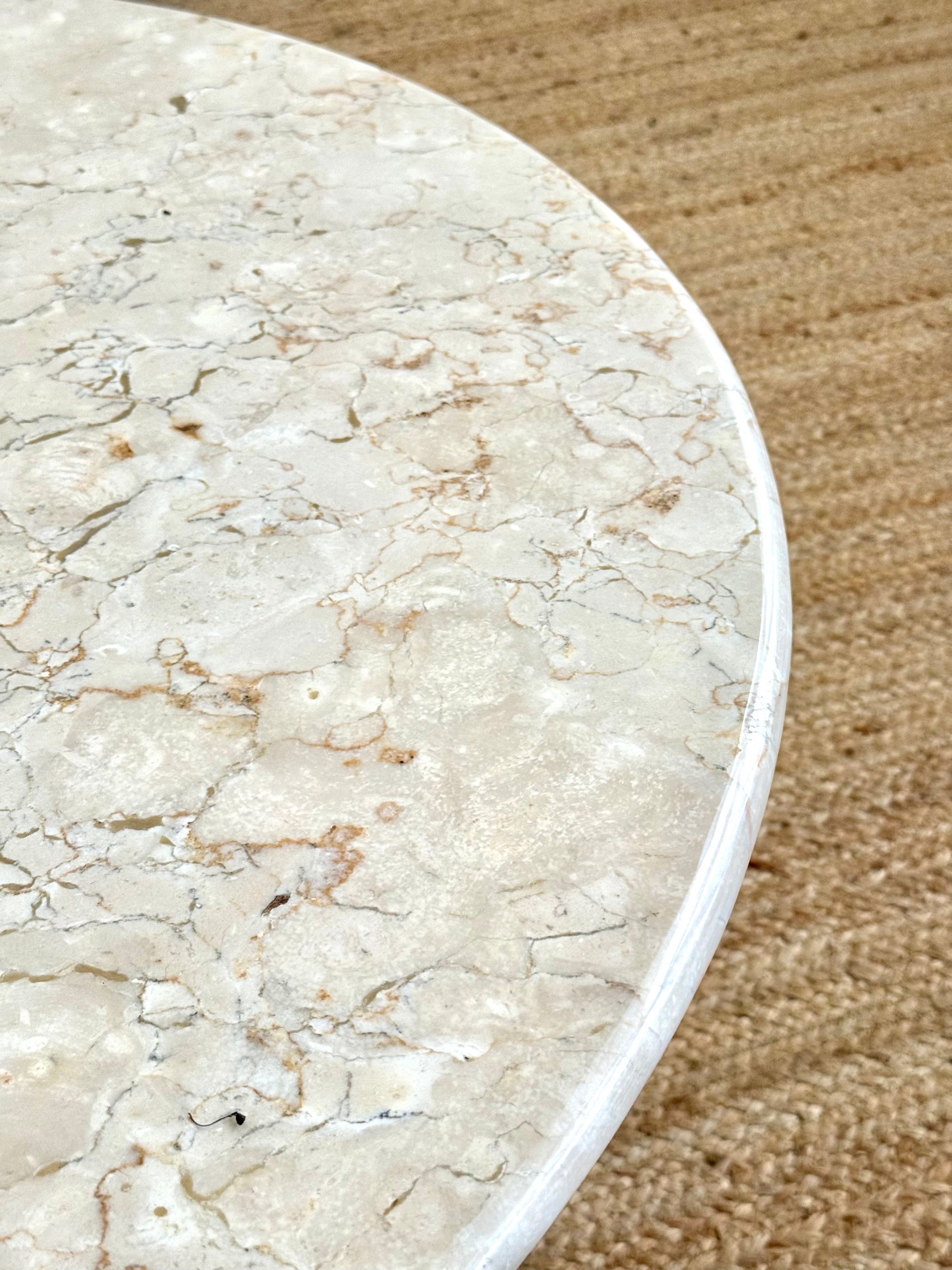 Close-up of a round table top made of polished beige and white marble with natural veining, set on a textured tan rug.