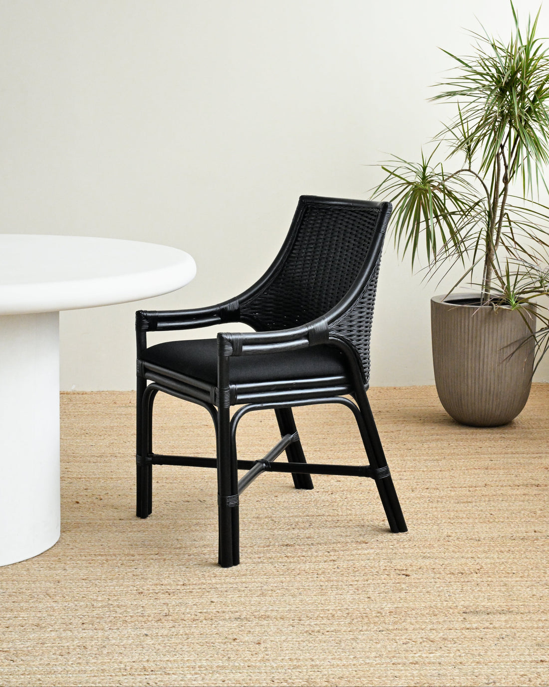 Black wicker chair next to a white table with a plant in the background