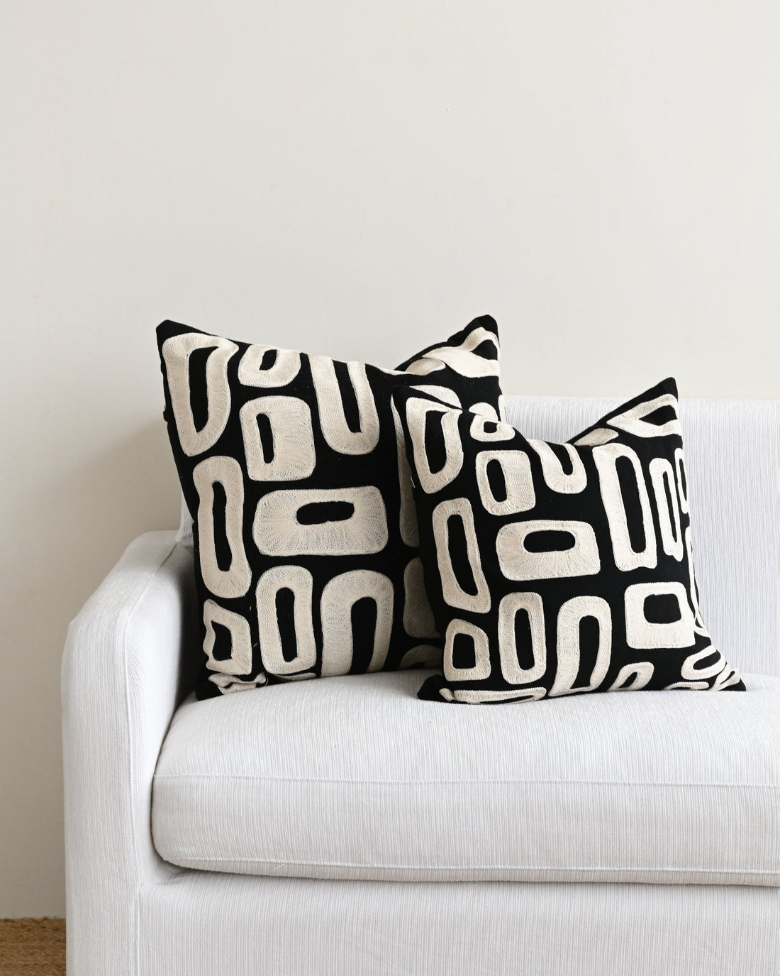 Two black and white patterned pillows on a white couch against a plain wall.