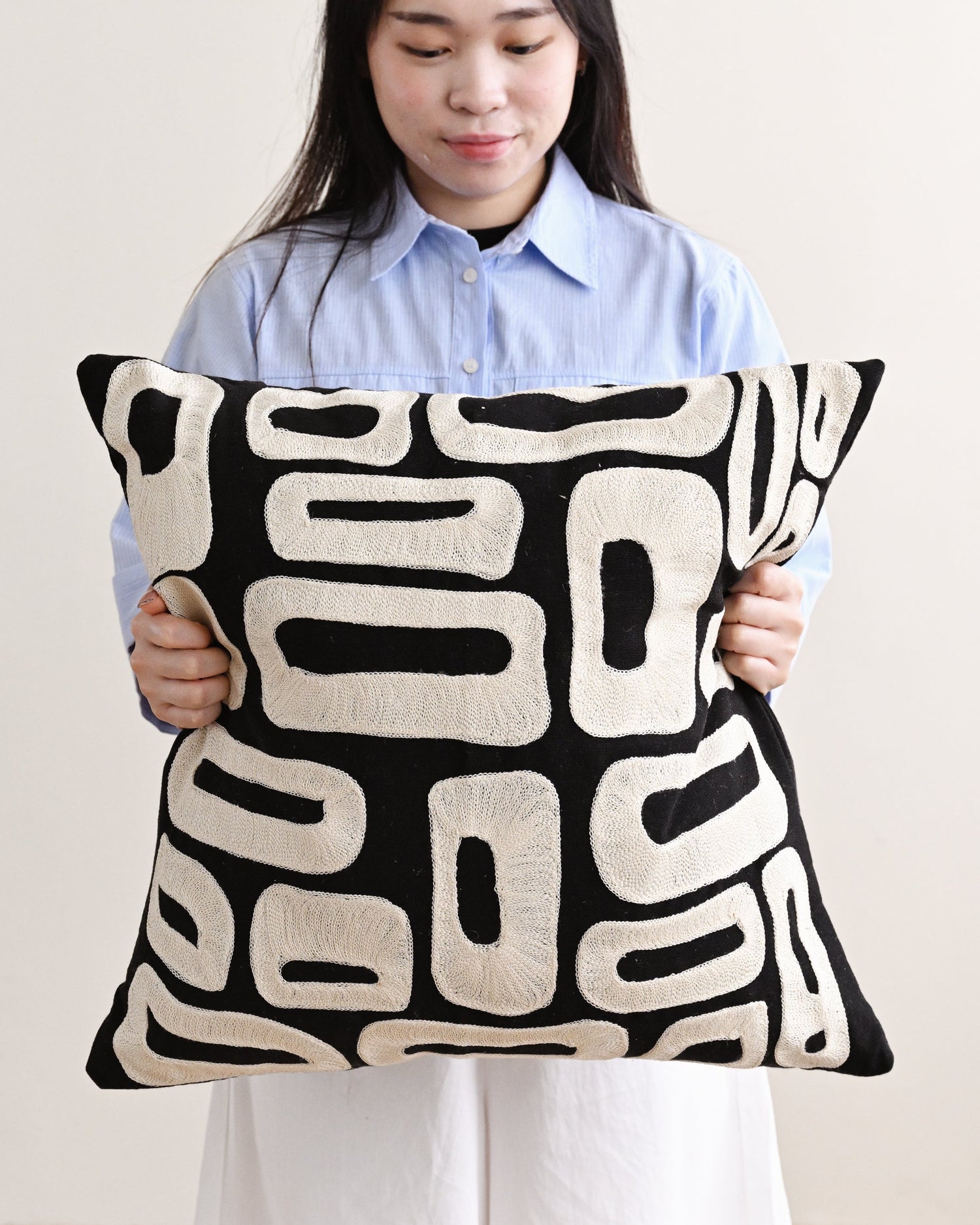 Person holding a black and white patterned pillow against a plain background