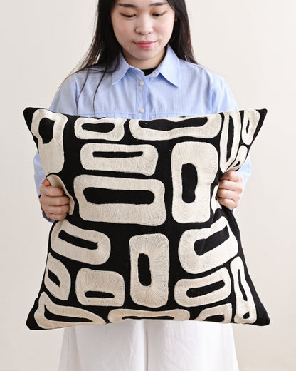 Person holding a black and white patterned pillow against a plain background