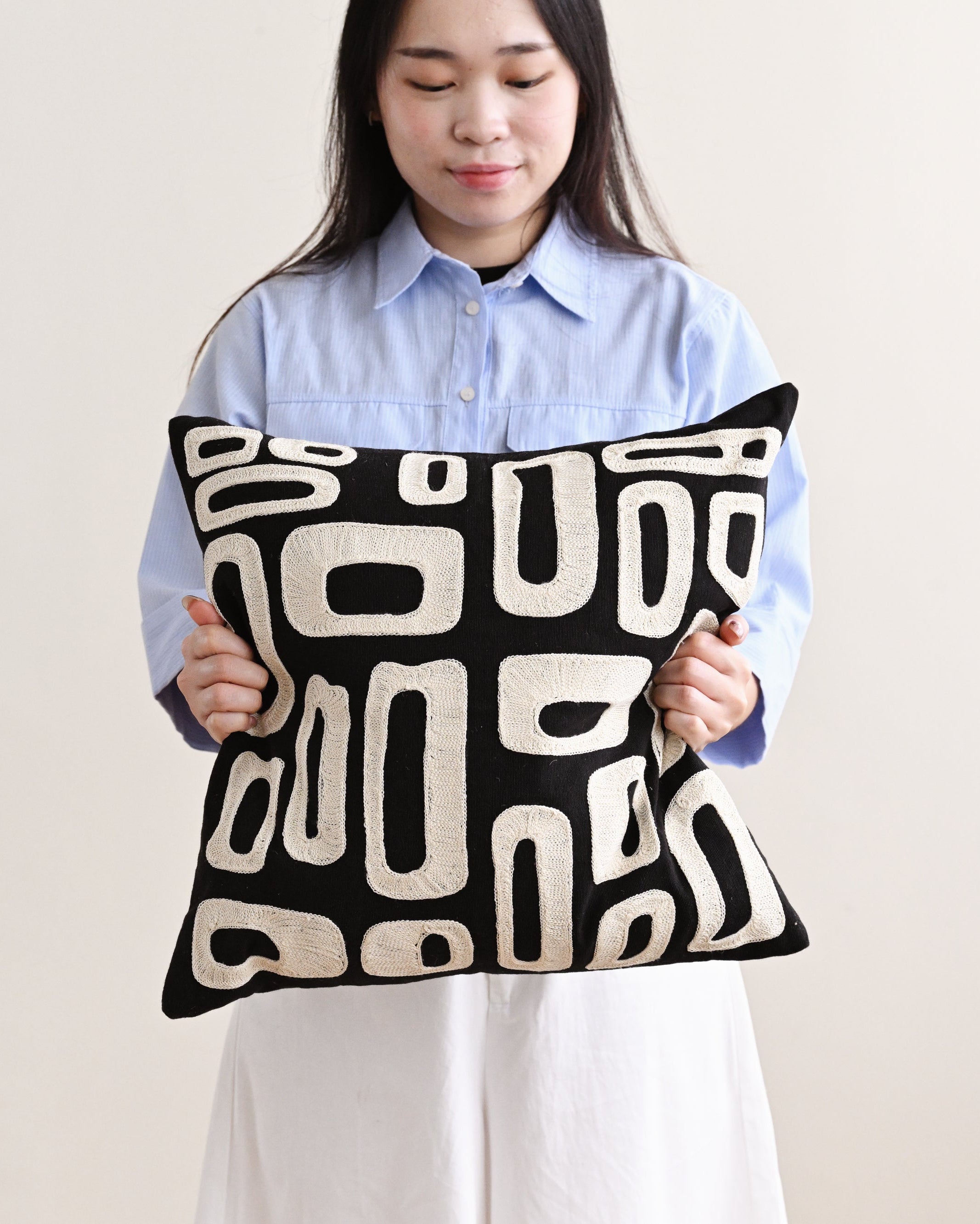 Woman holding a black pillow with white patterns against a plain background