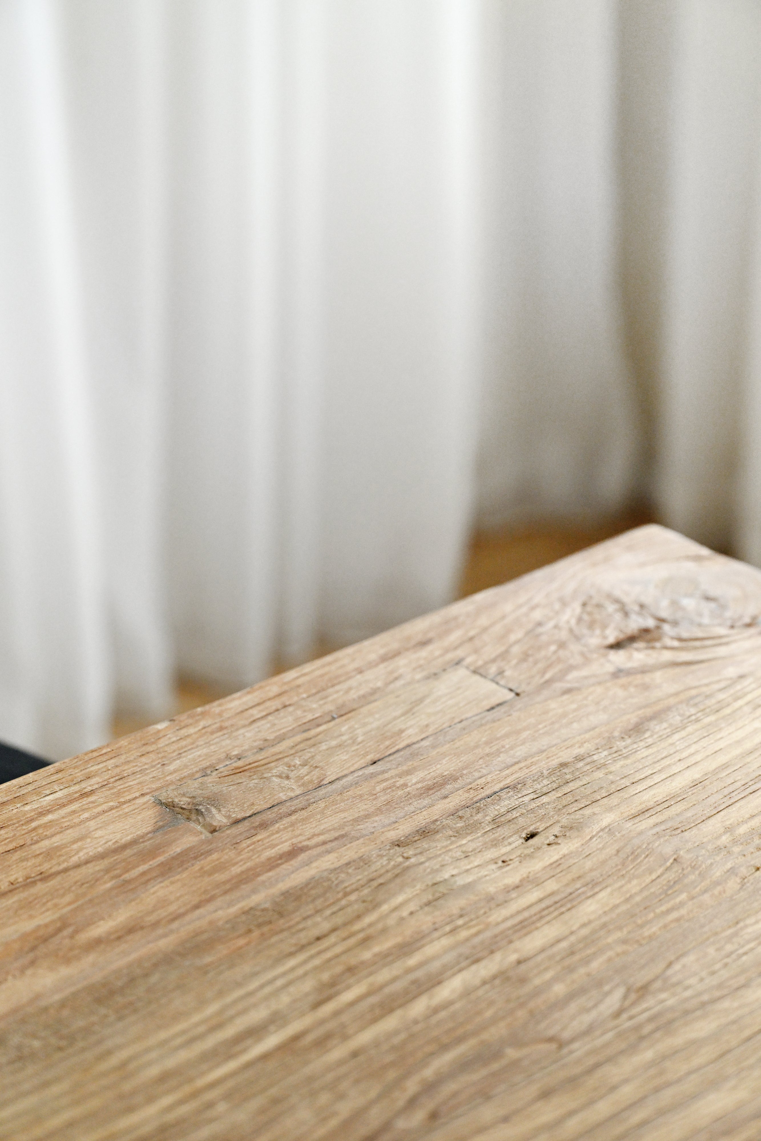 Close-up of a wooden surface with a blurred white curtain in the background