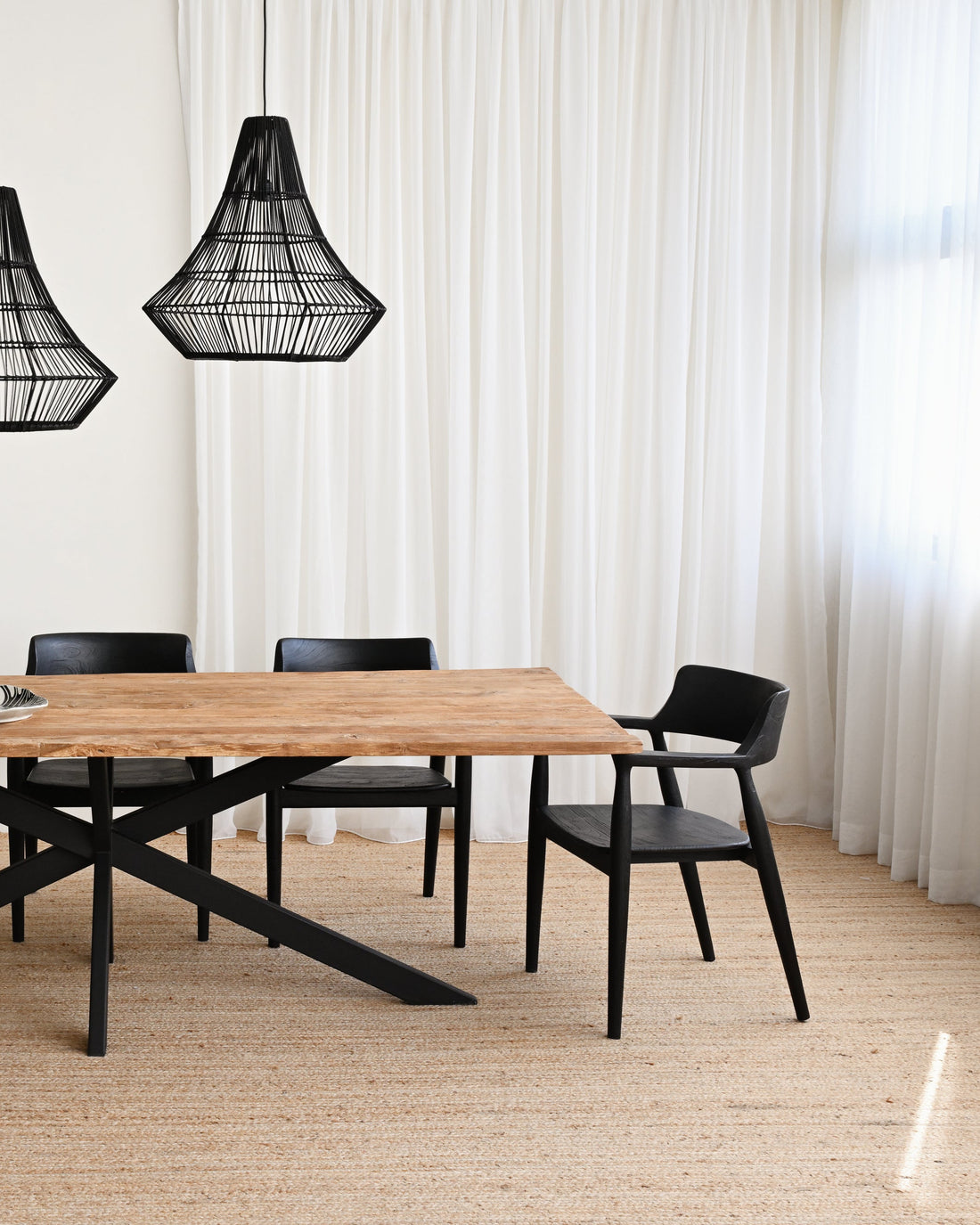 Dining table with chairs and black pendant lights in a room with white walls and wooden floor.