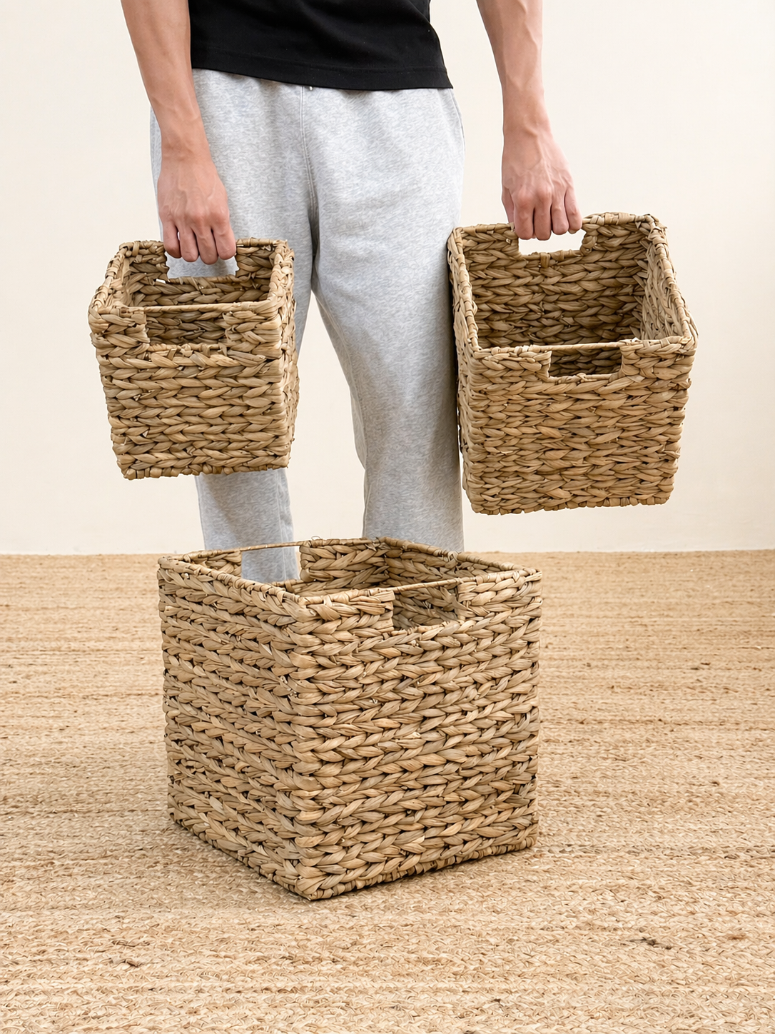 Person holding three woven baskets on a wooden floor.