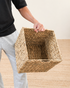 Person holding a woven basket on a wooden floor.